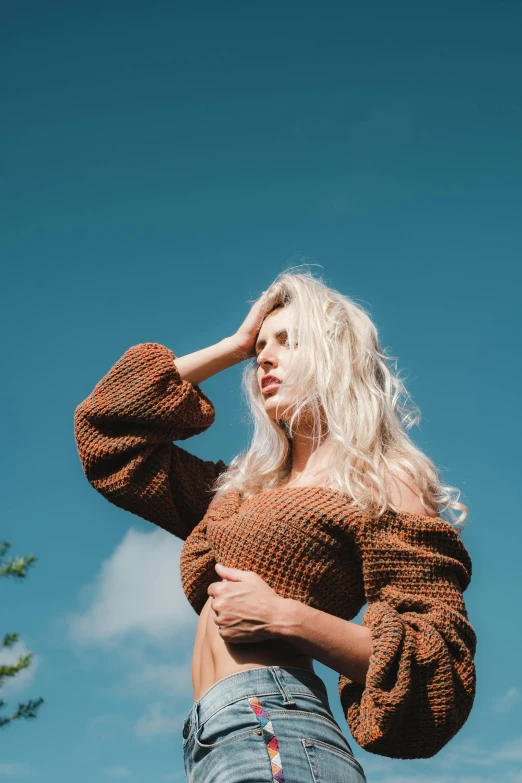 a woman standing in front of a blue sky, inspired by Elsa Bleda, unsplash, renaissance, brown sweater, ava max, summer day, caramel. rugged