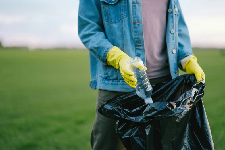 a person standing in a field holding a trash bag, bottle, black, sweeping, extra crisp image