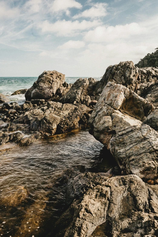 a man riding a surfboard on top of a rocky beach, stream of water, ((rocks)), unsplash 4k, erosion algorithm landscape