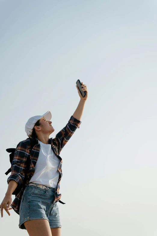 a woman flying a kite on top of a sandy beach, trending on pexels, happening, she is holding a smartphone, denim, looking upwards, androgynous person