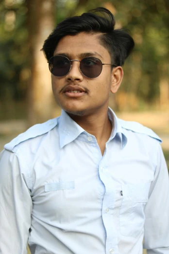 a man wearing sunglasses and a blue shirt, inspired by Bikash Bhattacharjee, androgynous face, he is about 20 years old | short, photgraph, assamese