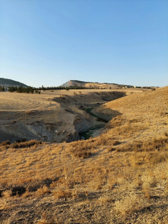 a man standing on top of a dry grass covered hillside, with a river running through it, slide show, agrigento, phone photo