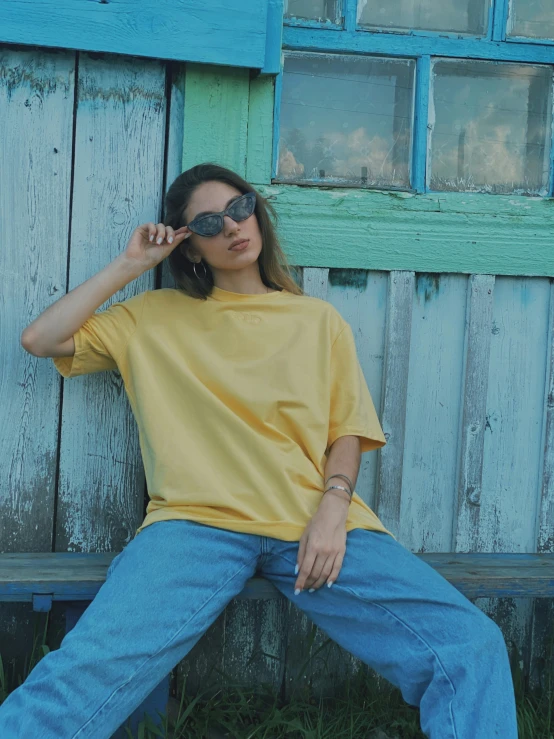 a woman sitting on top of a wooden bench, by Pablo Rey, trending on unsplash, hyperrealism, wearing a modern yellow tshirt, 1990s fashion, standing outside a house, promo image