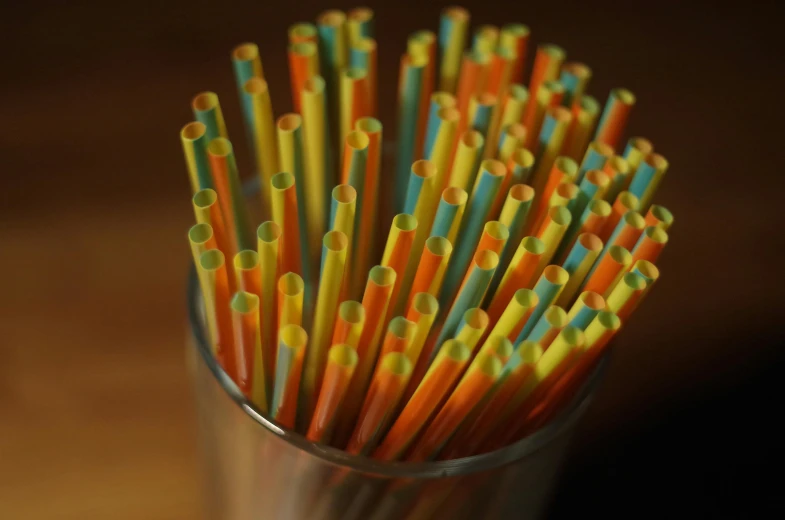 a glass filled with lots of colorful drinking straws, by Jessie Algie, chartreuse and orange and cyan, afternoon light, square, reuters