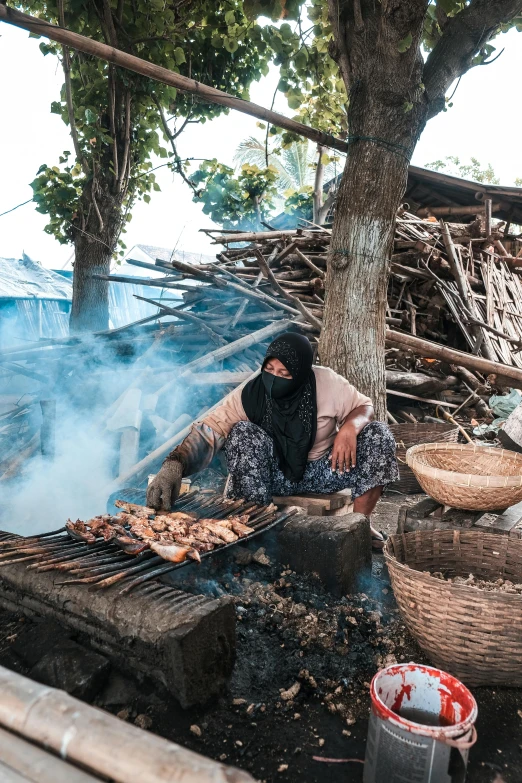 a woman cooking food on a grill under a tree, by Daniel Lieske, pexels contest winner, hurufiyya, burning village, eating meat, island, praying with tobacco
