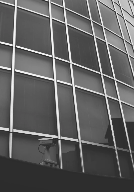 a black and white photo of a tall building, a black and white photo, inspired by Vivian Maier, unsplash, modernism, glass wall, security cam, square, full of glass. cgsociety