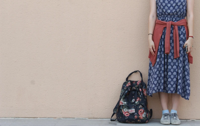 a woman standing next to a wall with a backpack, unsplash, renaissance, background image, floral clothes, black, style of yoshii chie