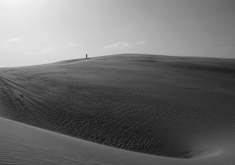 a lone person standing on top of a sand dune, a black and white photo, by Matthias Weischer, unsplash contest winner, in the desert beside the gulf, today\'s featured photograph 4k, flat wastelands, alone!!