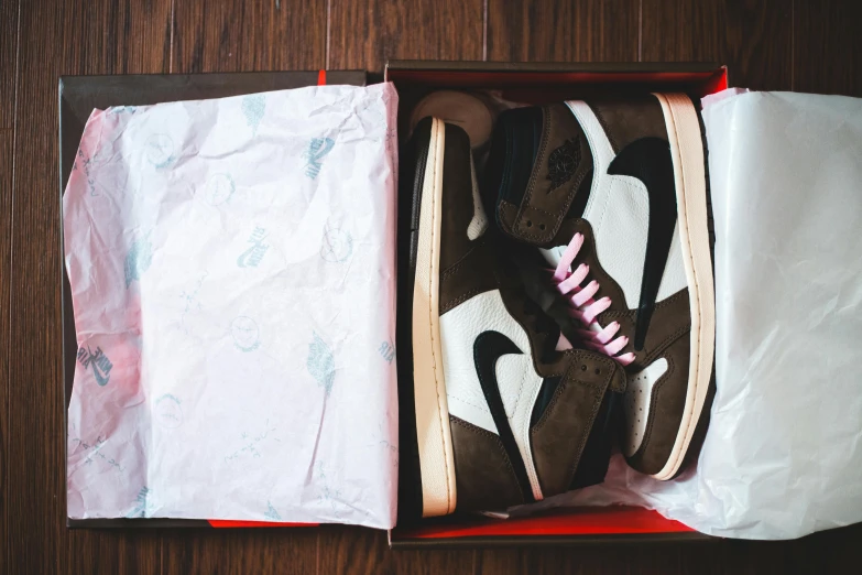 a pair of shoes in a box on a wooden floor, inspired by Jordan Grimmer, unsplash, air jordan 1 high, brown and pink color scheme, uniform off - white sky, brown