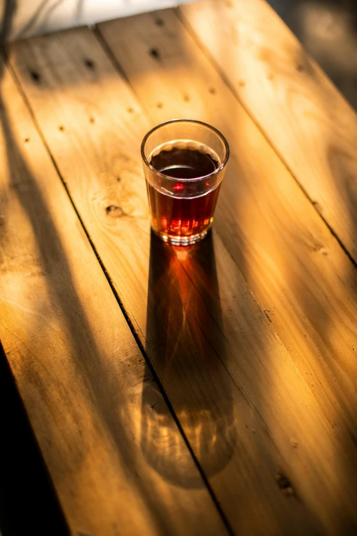 a glass of beer sitting on top of a wooden table, amaro, dappled light, knockout punch, dark red