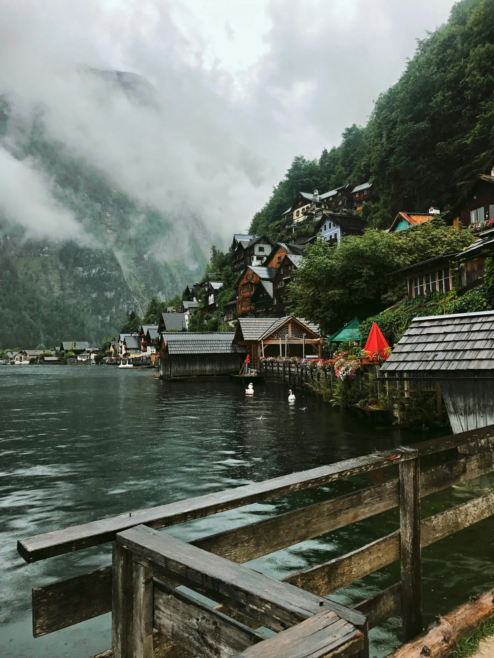 a person standing on a dock next to a body of water, quaint village, alpine architecture, rainy outside, instagram post