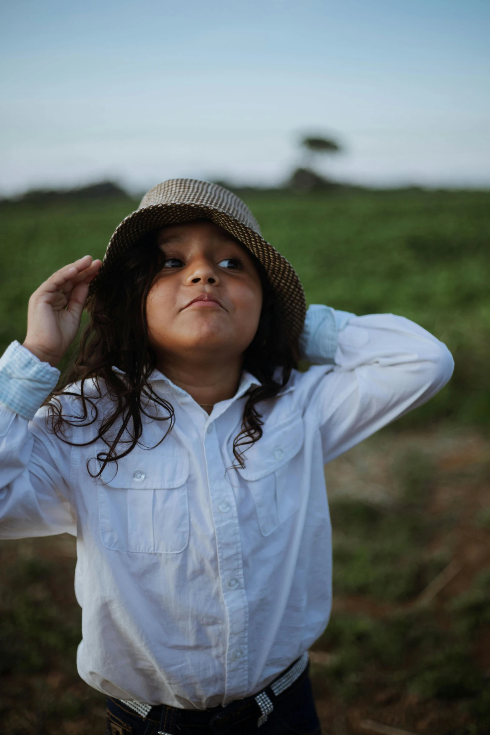 a little girl standing in a field with a hat on, inspired by Dorothea Lange, unsplash, wearing a white button up shirt, an olive skinned, lit up, still from a music video