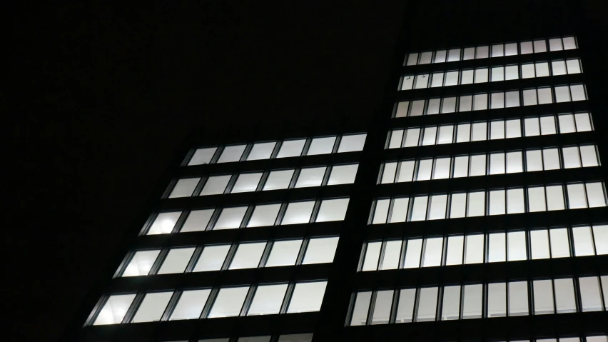 a tall building with lots of windows lit up at night, inspired by Andreas Gursky, unsplash, brutalism, steel window mullions, dark and white, square shapes, low angle photograph