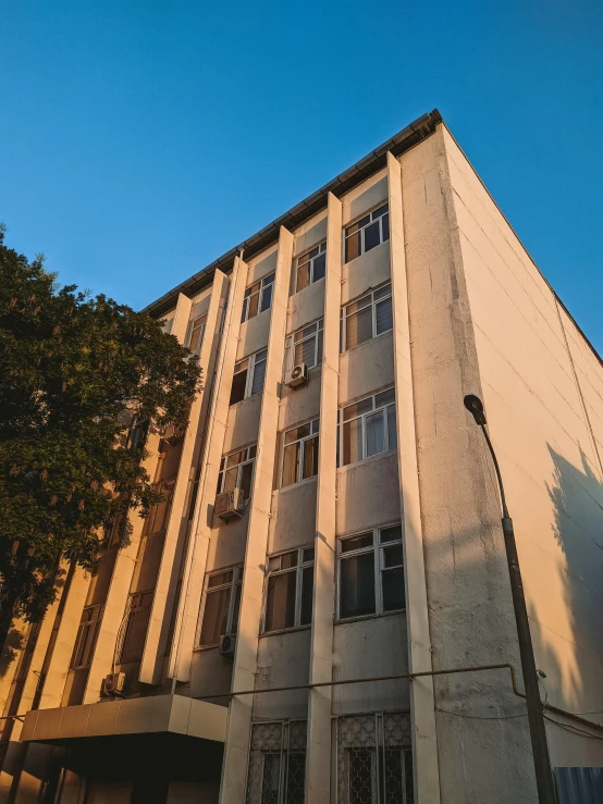 a tall building sitting on the side of a street, a photo, unsplash, bengal school of art, background image, soviet brutalism, golden hour photo, фото девушка курит