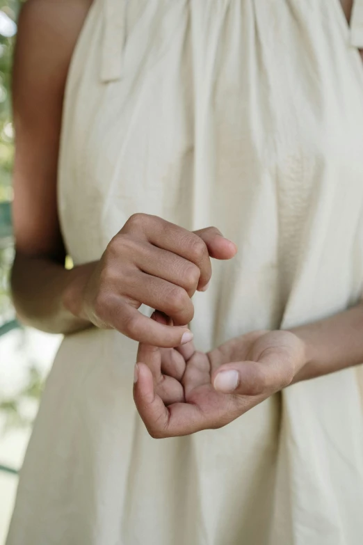 a woman in a white dress holding something in her hands, by Jessie Algie, unsplash, unclipped fingernails, organic detail, photo of a black woman, warm weather