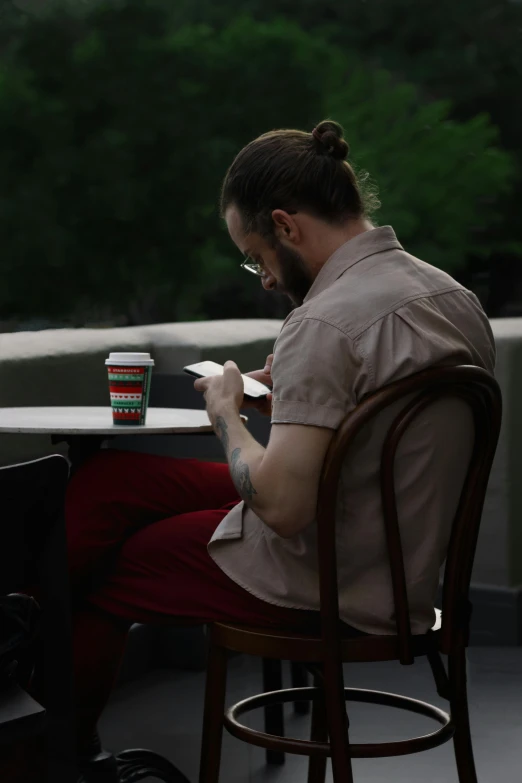 a man sitting at a table with a cup of coffee, inspired by Seb McKinnon, ponytail and beard, **cinematic, lachlan bailey, starbucks