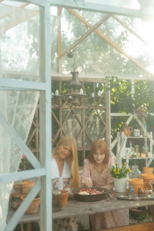 a couple of women sitting at a table in a greenhouse, inspired by Elsa Beskow, pexels contest winner, home video footage, summer lighting, movie footage, panoramic view of girl