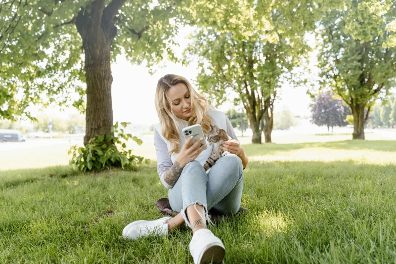 a woman sitting in the grass using a cell phone, by Julia Pishtar, pexels contest winner, happening, holding a cat, blonde women, white, avatar image