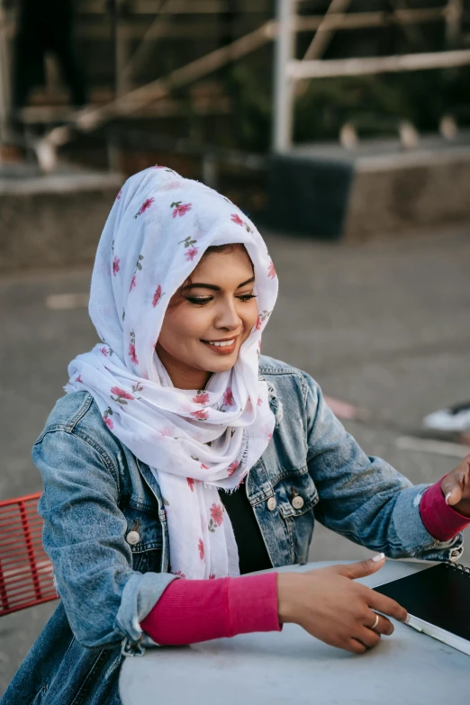 a woman sitting at a table with a laptop, hurufiyya, patterned scarf, 2019 trending photo, outdoor photo, checking her phone