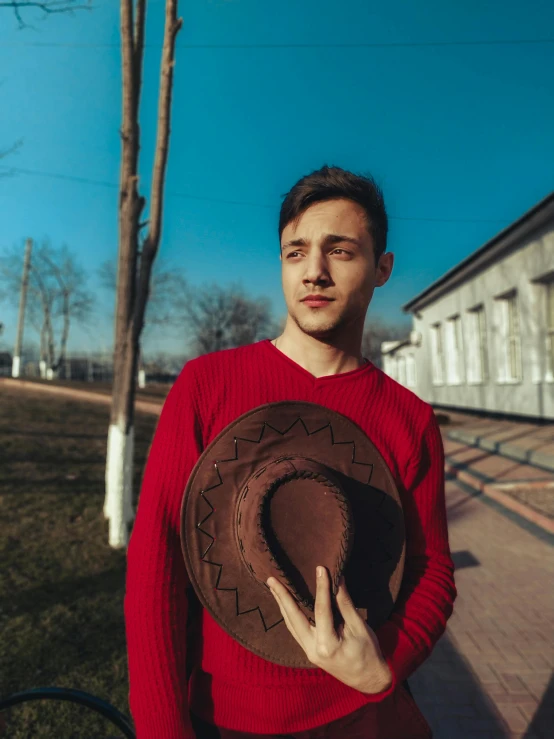 a man in a red sweater holding a brown hat, inspired by Alexey Venetsianov, pexels contest winner, non binary model, ukrainian, background image, 2019 trending photo