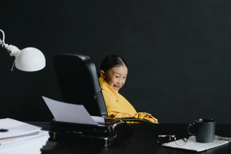 a woman sitting at a desk working on a laptop, an album cover, inspired by Ye Xin, pexels contest winner, happy kid, girl in suit, black and yellow, office furniture