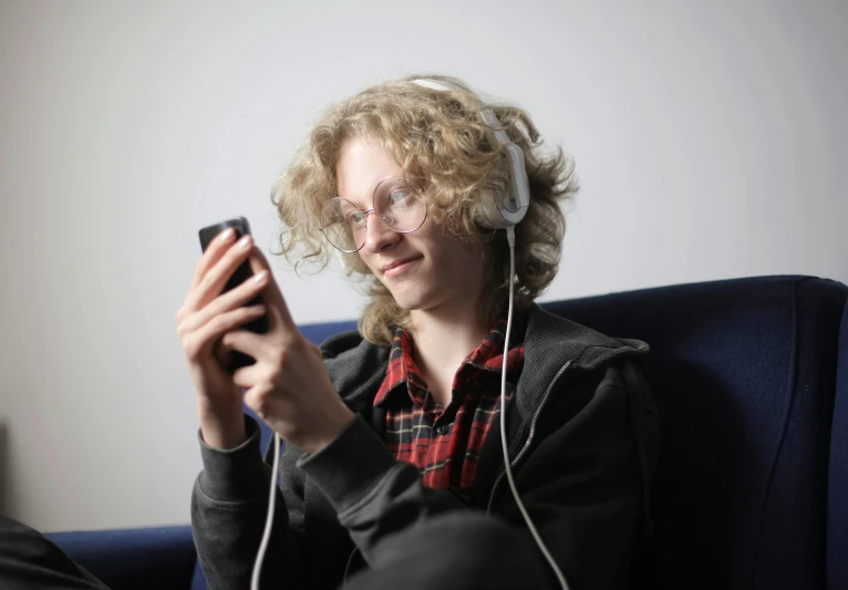 a woman sitting in a chair holding a cell phone, an album cover, by Edward Clark, pexels, pale skin curly blond hair, male teenager, gaming headset, looking at his phone