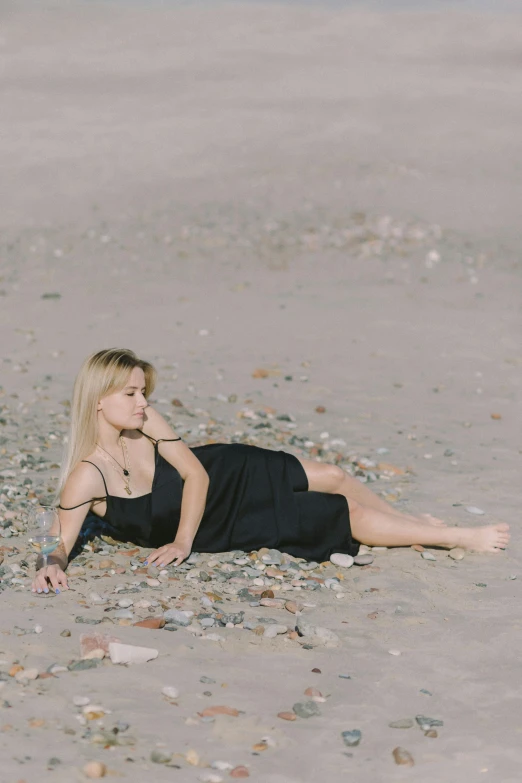 a woman laying on top of a sandy beach, unsplash, realism, wearing black dress, a blond, gravels around, 15081959 21121991 01012000 4k