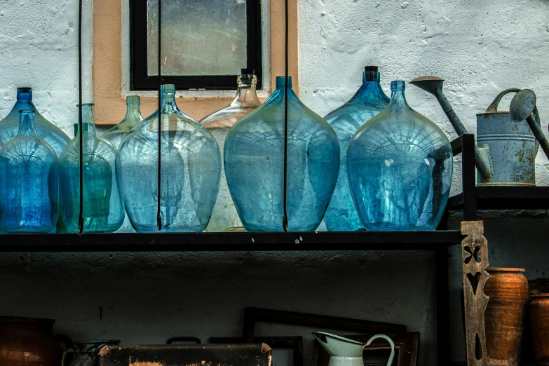 a shelf filled with blue glass bottles next to a window, trending on unsplash, arte povera, large jars on shelves, paul barson, dressed in a worn, in a row