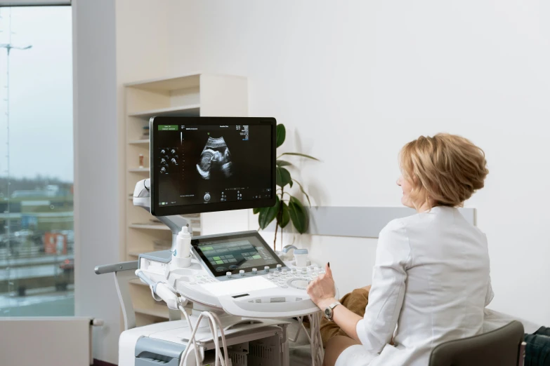 a woman sitting in a chair in front of a computer, digital medical equipment, femme fetal, ultrastation hq, grey