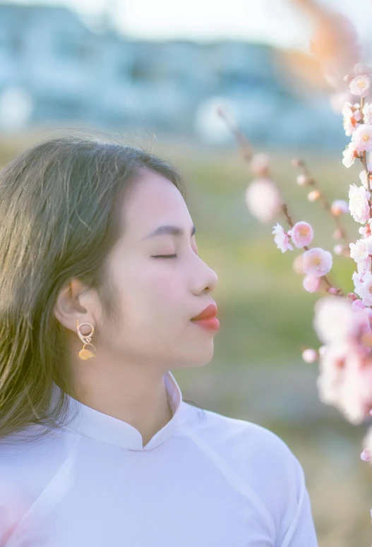 a woman standing in front of a tree with pink flowers, inspired by Cui Bai, trending on unsplash, aestheticism, wearing pearl earrings, with closed eyes, vietnamese woman, trending on cgstation