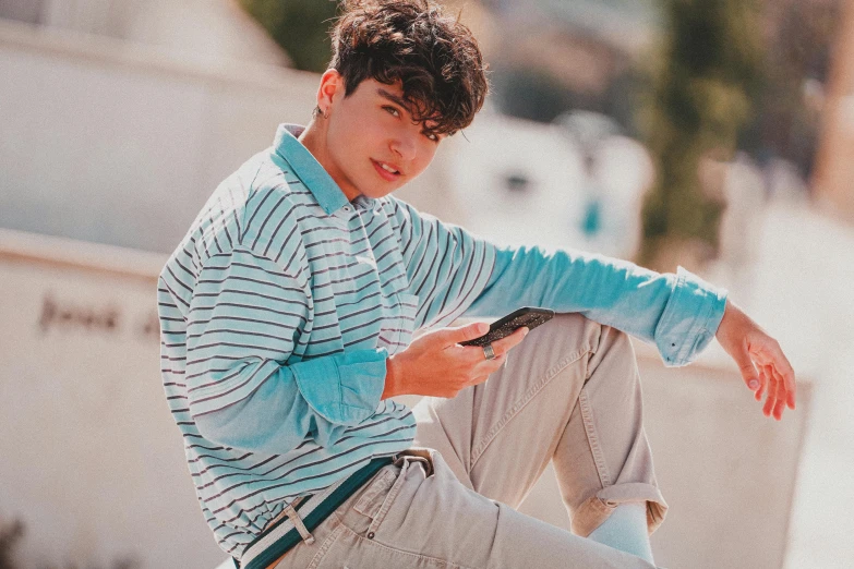 a young man sitting on top of a skateboard, an album cover, inspired by John Luke, trending on pexels, realism, white and teal garment, looking at his phone, wearing stripe shirt, siwoo kim