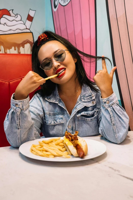 a woman sitting at a table with a plate of food, inspired by Pia Fries, pexels contest winner, pop art, hot dog, wearing small round glasses, teenage vanessa morgan, rockabilly style