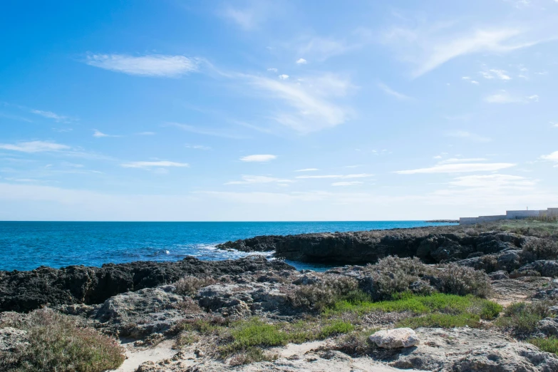 a man riding a surfboard on top of a rocky beach, clear blue skies, rock pools, distant ocean, varadero beach