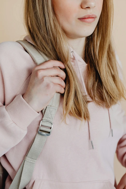 a woman in a pink hoodie poses for a picture, by Nina Hamnett, trending on pexels, school bag, pale pastel colours, taupe, straps