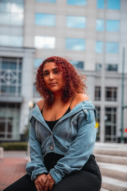 a woman sitting on a bench in front of a building, by Washington Allston, trending on pexels, renaissance, curly copper colored hair, ameera al-taweel, wearing a jeans jackets, serious look