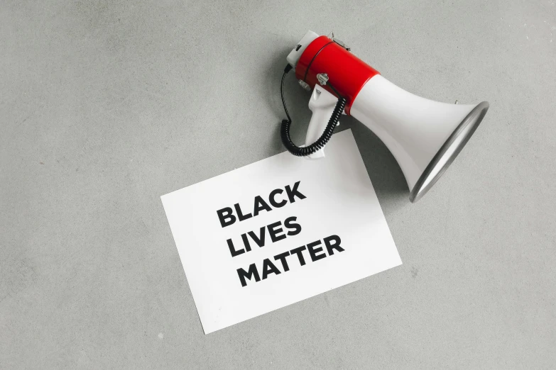 a red and white megaphone next to a piece of paper that says black lives matter, a black and white photo, by Julia Pishtar, trending on pexels, b