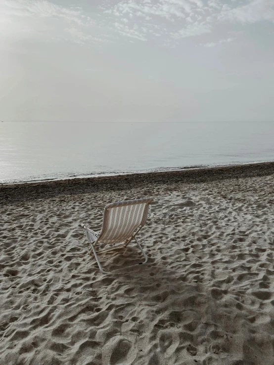 a beach chair sitting on top of a sandy beach, inspired by Wilhelm Hammershøi, unsplash contest winner, romanticism, low quality photo, early evening, grey, wide high angle view