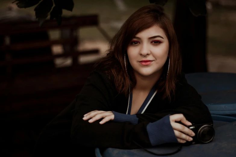 a woman sitting at a table with a camera, an album cover, inspired by Glòria Muñoz, pexels contest winner, confident smirk, in a navy blue sweater, charli bowater, plus size