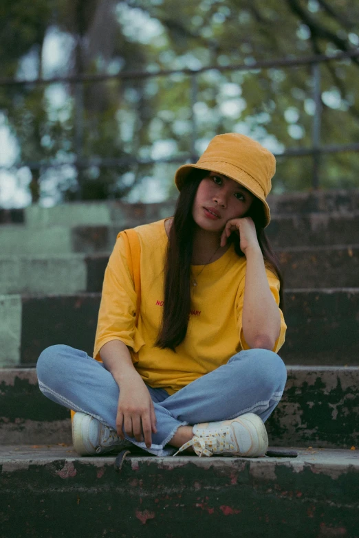 a woman sitting on some steps talking on a cell phone, inspired by Elsa Bleda, pexels contest winner, yellow cap, asian girl, bucket hat, wearing a modern yellow tshirt