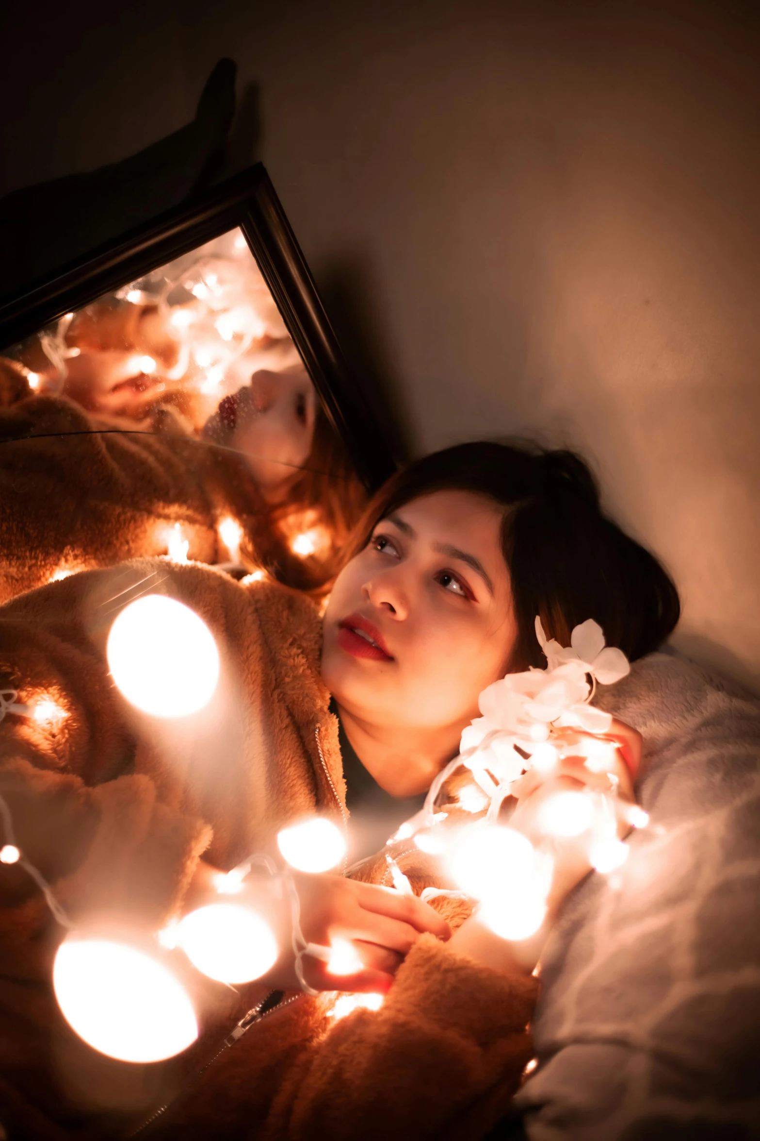 a woman laying in bed with christmas lights around her, a picture, inspired by Elsa Bleda, pexels contest winner, looking in a mirror, asian woman, lights with bloom, awkward