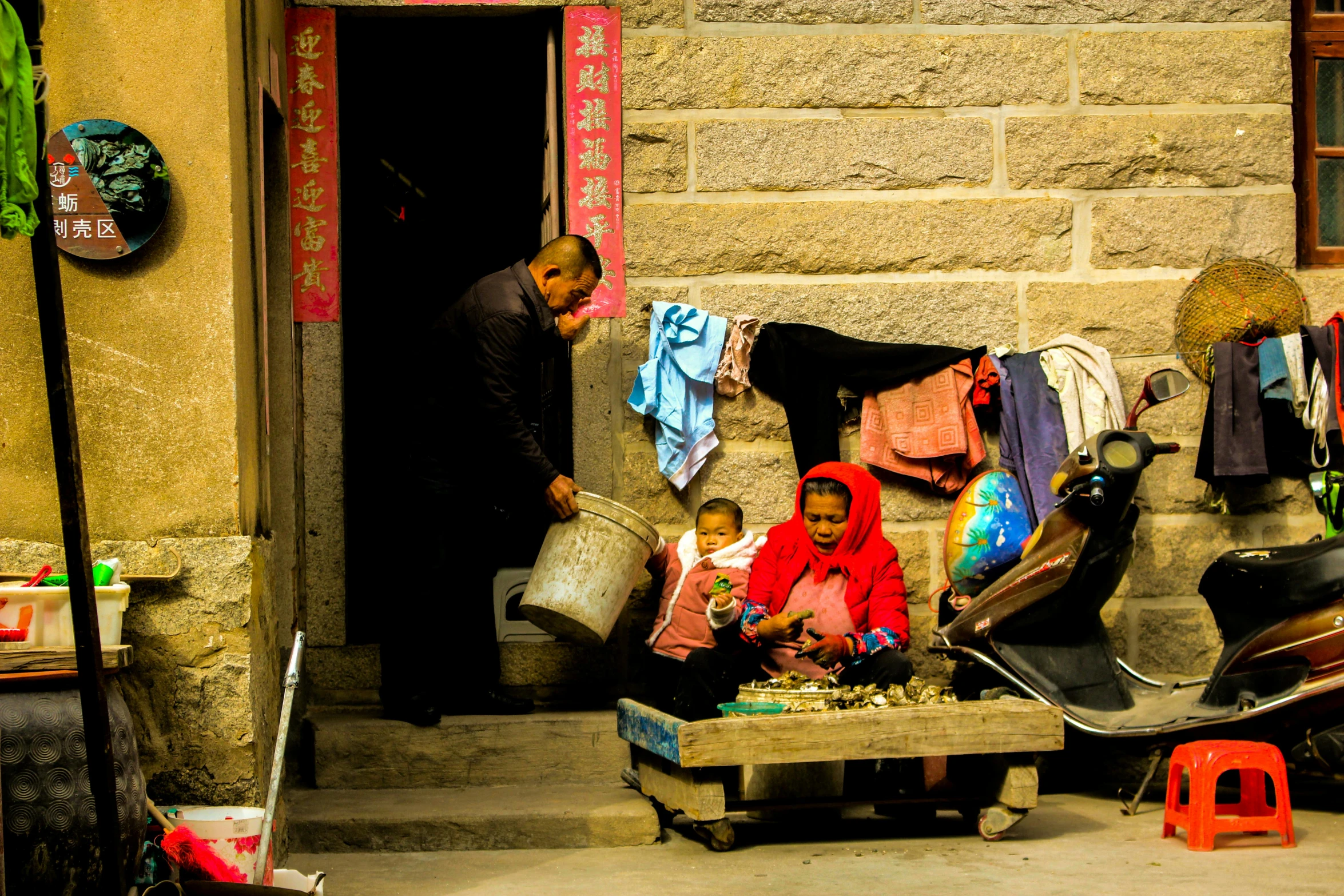 a group of people sitting in front of a building, by Peter Churcher, pexels contest winner, nezha, selling his wares, warm glow, family friendly