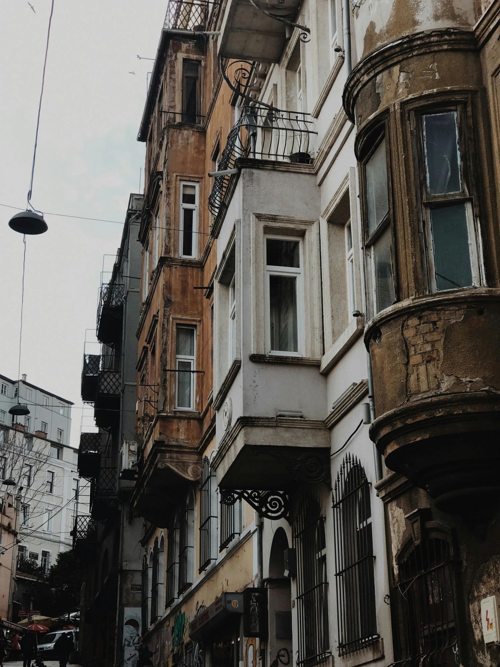 a group of people walking down a street next to tall buildings, a photo, inspired by Niyazi Selimoglu, renaissance, aged and weathered, trending on vsco, wrought iron architecture, close - up photograph