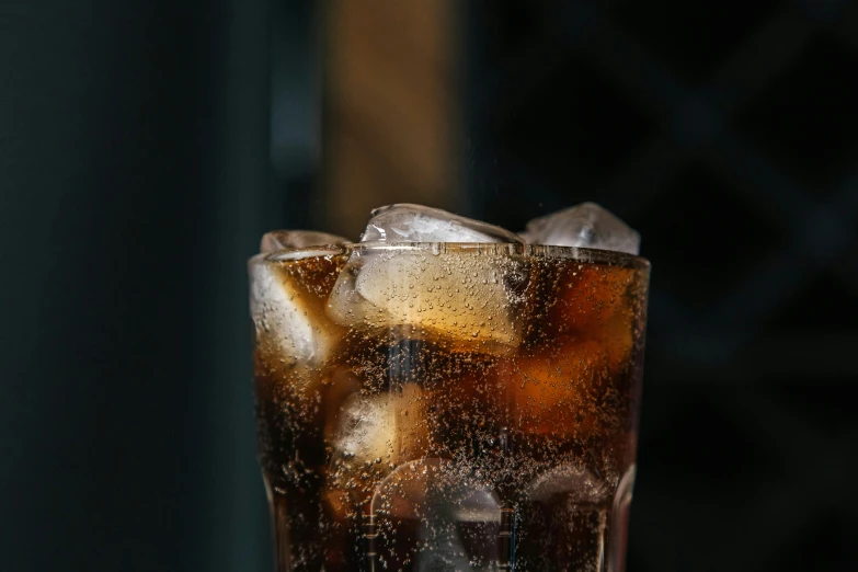 a glass of soda sitting on top of a table, inspired by Dorothy Coke, pexels, panel of black, close up shot from the side, cold drinks, brown