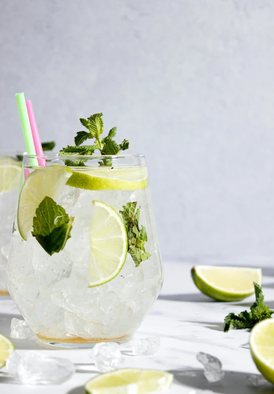 two glasses filled with ice and lime slices, unsplash, photorealism, mint higlights, on a pale background, profile image, with a straw