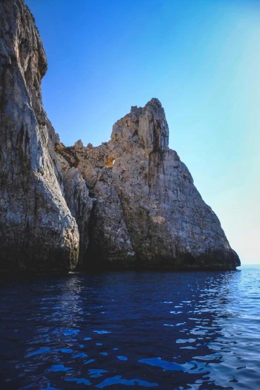 a rock formation in the middle of a body of water, piroca, steep cliffs, slide show, atmospheric photo