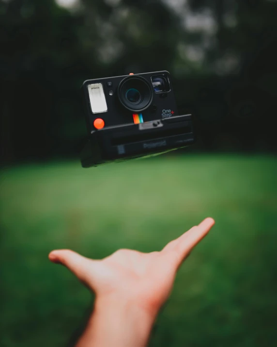 a person holding a camera in their hand, a polaroid photo, pexels contest winner, leaping towards viewer, toy camera, nature photo, waving