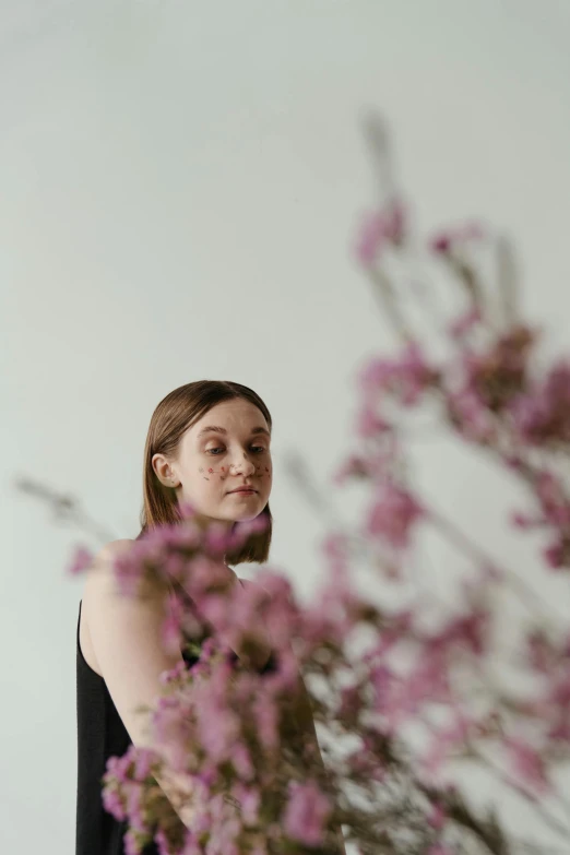 a woman standing in front of a vase of flowers, an album cover, by Sara Saftleven, pexels contest winner, beautiful taissa farmiga, kirsi salonen, branches sprouting from her head, looking to the side off camera