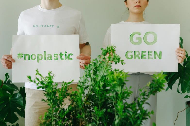 two people holding up signs that say go plastic green, trending on unsplash, plasticien, woman made of plants, low quality photo, background image