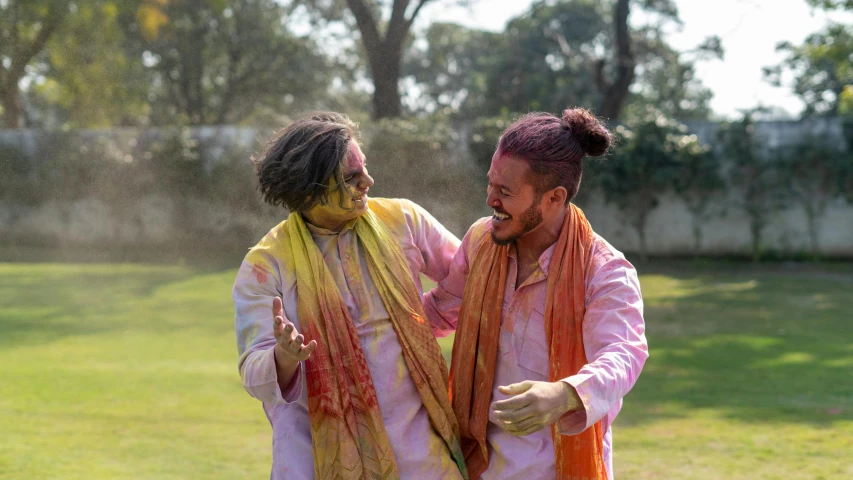 a couple of men standing on top of a lush green field, pexels contest winner, bengal school of art, fully covered in colorful paint, head bent back in laughter, wearing traditional garb, fall season