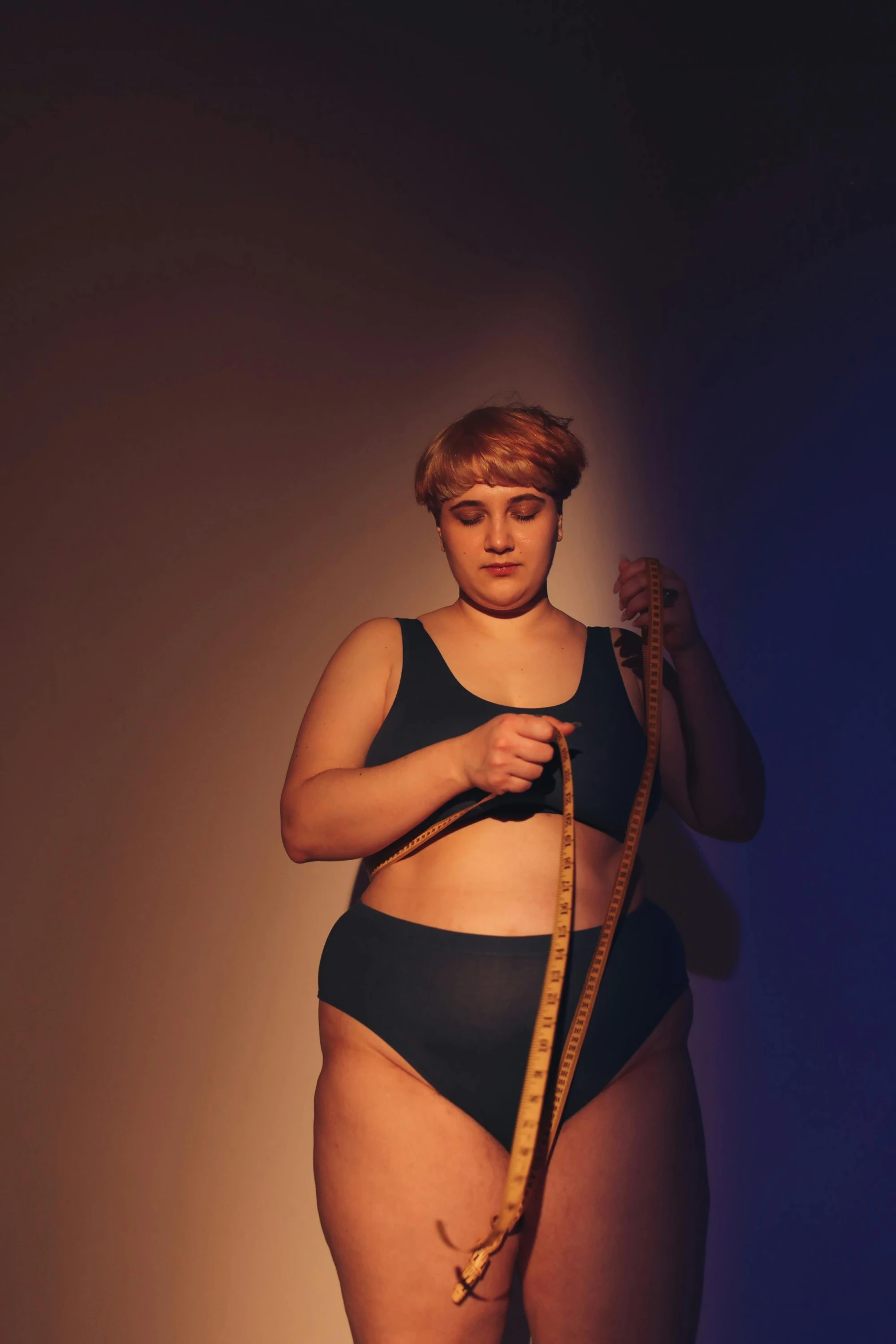 a woman with a measuring tape around her waist, by Arabella Rankin, non-binary, sport bra and dark blue shorts, rubenesque, in the spotlight